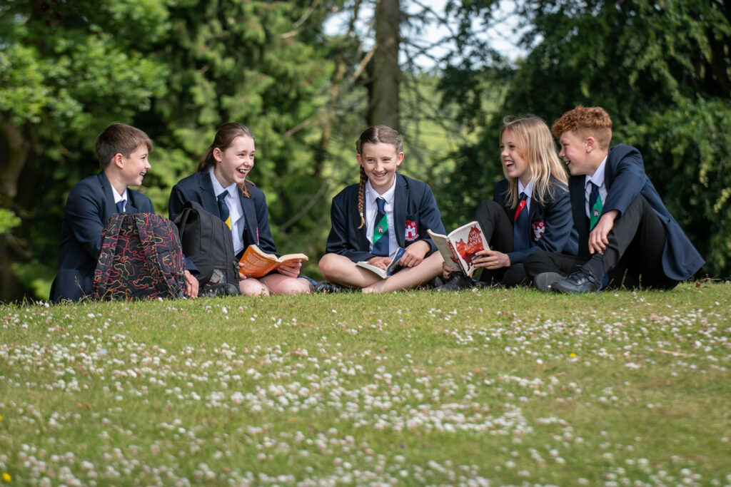 five students sitting on the grass laughing and smiling