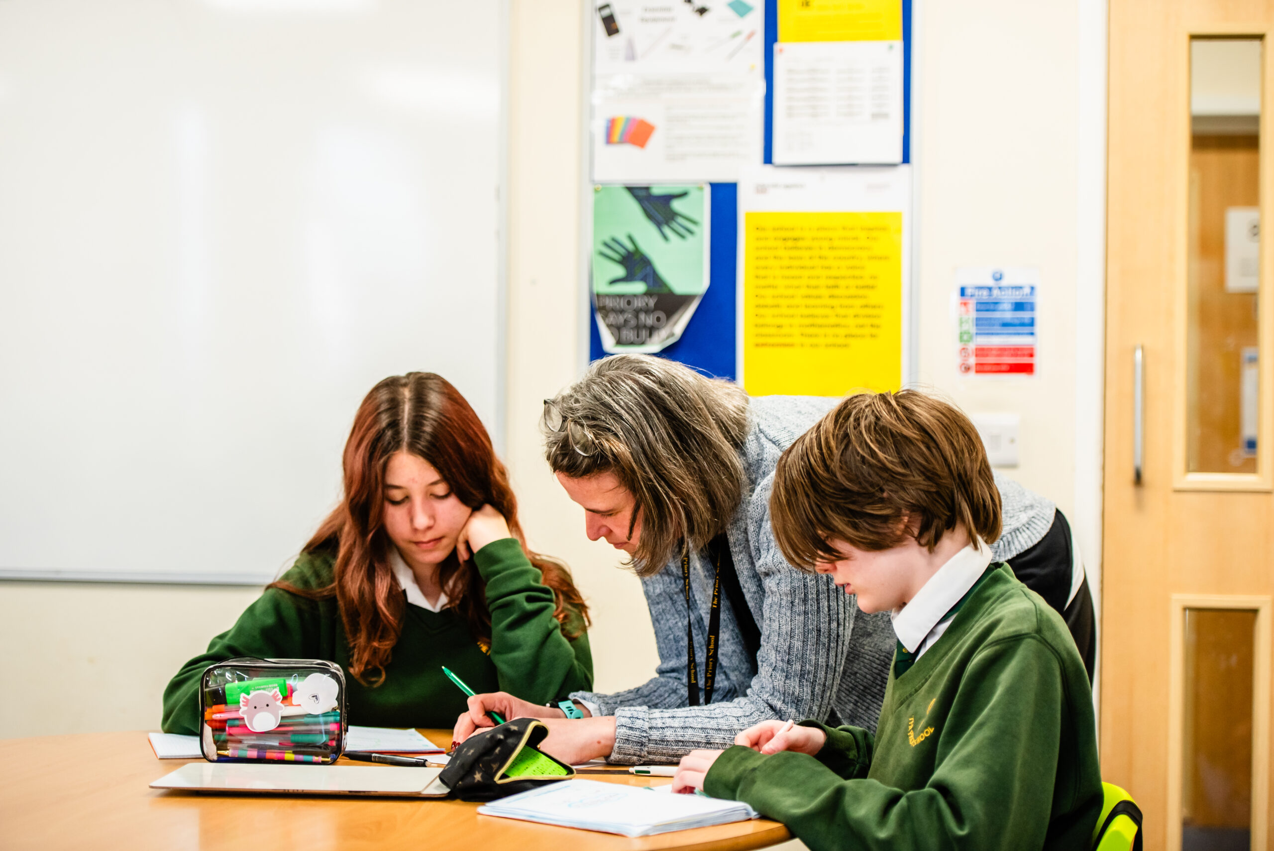 Teacher and two pupils at a table with posters in the background
