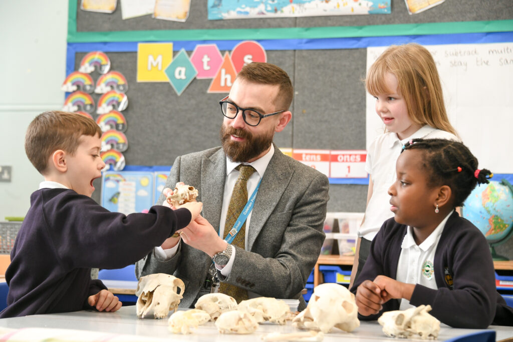 A teacher and three pupils examine animal skulls in a decorated classroom.
