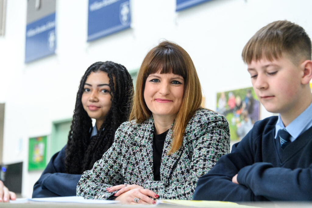 Three people seated at a table, posters are visible on the wall behind them.