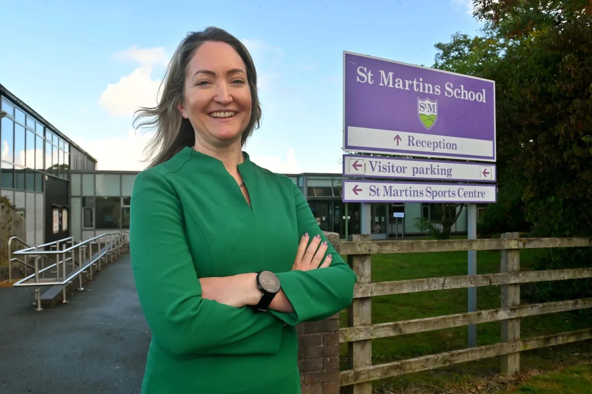 Female headteacher in green top standing outside of school next to purple school sign